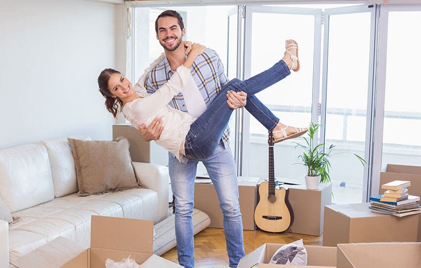The image depicts a blue Hire Man and Van removal van parked on a residential driveway in Lossiemouth, with its side door open, revealing a large load of assorted waste materials. In the foreground, there are numerous black plastic garbage bags tightly packed and stacked, some partially torn, alongside flattened cardboard boxes and loose plastic items. Nearby, a white plastic garden chair is partially visible leaning against the vehicle. The concrete driveway surface shows slight wear, with a wooden fence and a section of brick wall lining the background, suggesting a domestic property setting. The surrounding environment appears to be a typical suburban suburban street scene, with muted natural lighting indicating an overcast day. The van's exterior is clean and features the company's branding subtly visible. The scene captures a routine rubbish removal operation, with the waste ready for collection service, reflecting the local context of waste clearance in Lossiemouth, postcodes IV31.
